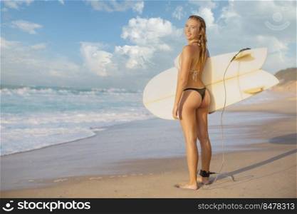 Beautiful blonde girl at the beach holding a surfboard