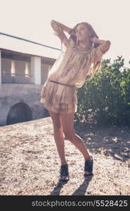 Beautiful blonde girl, dressed with a beige dress, standing in a rural bridge