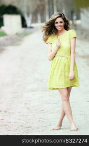 Beautiful blonde girl, dressed with a beige dress, standing in rural road