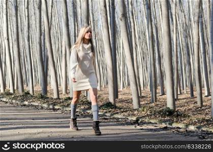 Beautiful blonde girl, dressed with beige dress, walking in a rural road