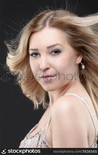 Beautiful blonde girl looks at camera, dark background