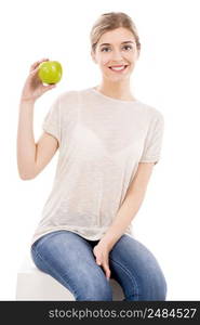 Beautiful blonde girl sitting and holding a green apple, over a white background