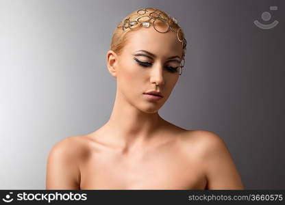 beautiful blonde girl with clean skin, nude shoulders and cute make-up wearing gold jewelry on the head. Gray background