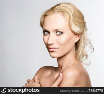 beautiful blonde girl with nudes shoulders and natural makeup, she is turned of three quarters at right with crossed arms, looks in to the lens and smiles