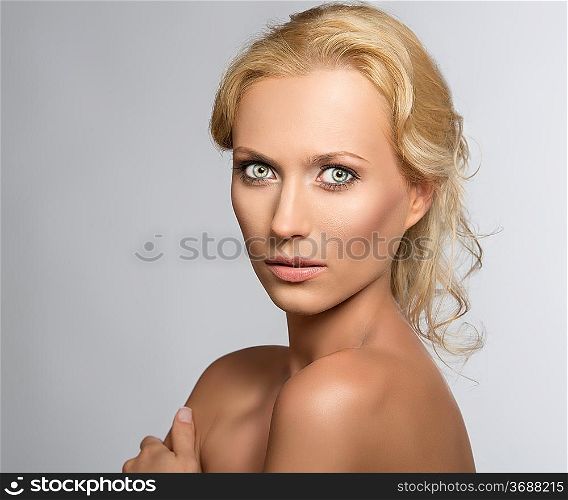 beautiful blonde girl with nudes shoulders and natural makeup, she is turned of three quarters at right, looks in to the lens and her left hand is on the right shoulder