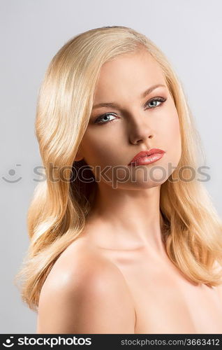 beautiful blonde girl with smooth hair and naked shoulders, her body is turned of three quarters at left and she looks in to the lens