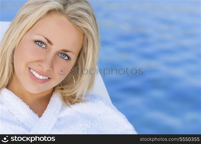 Beautiful blonde girl young woman in white spa robe with natural blue water background