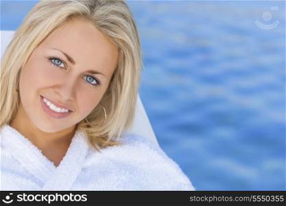 Beautiful blonde girl young woman in white spa robe with natural blue water background