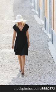 Beautiful blonde girl young woman walking in white hat and little black dress