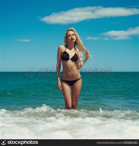 Beautiful blonde lady in a black swimsuit at the sea
