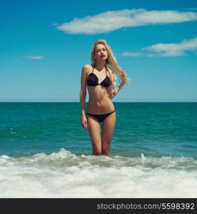 Beautiful blonde lady in a black swimsuit at the sea