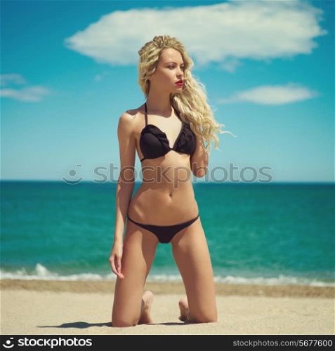 Beautiful blonde lady in a black swimsuit at the sea