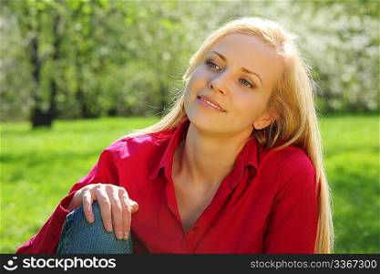 beautiful blonde sits on grass in park in spring