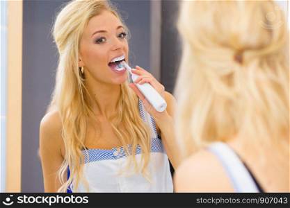 Beautiful blonde woman brushing her teeth using electric toothbrush having fun. Hygiene, body care concept.. Woman using electric toothbrush