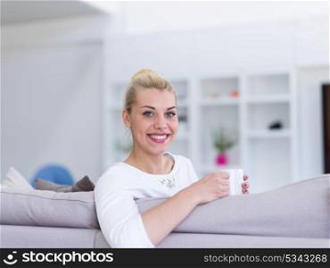 beautiful blonde woman enjoying a cup of coffee while sitting on a sofa in her apartment