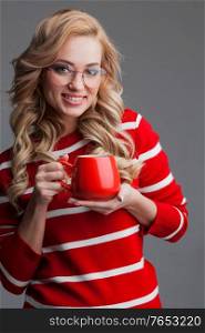 Beautiful blonde woman in glasses holding red cup of drink Christmas Valentines day concept. Beautiful woman in glasses holding red cup