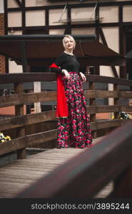 Beautiful blonde woman in red dress posing on wooden bridge at old european city