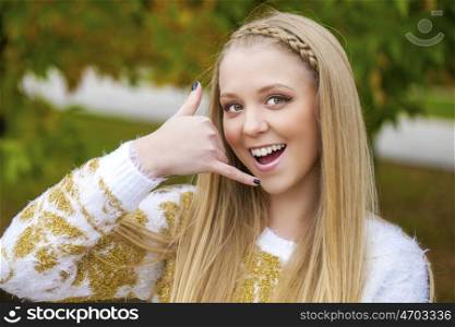 Beautiful blonde woman making a call me gesture, outdoors autumn park
