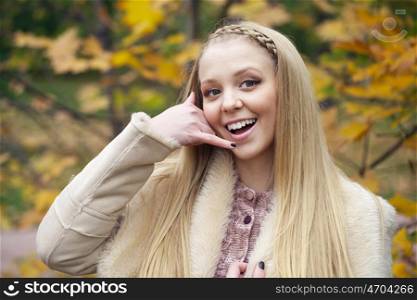 Beautiful blonde woman making a call me gesture, outdoors autumn park