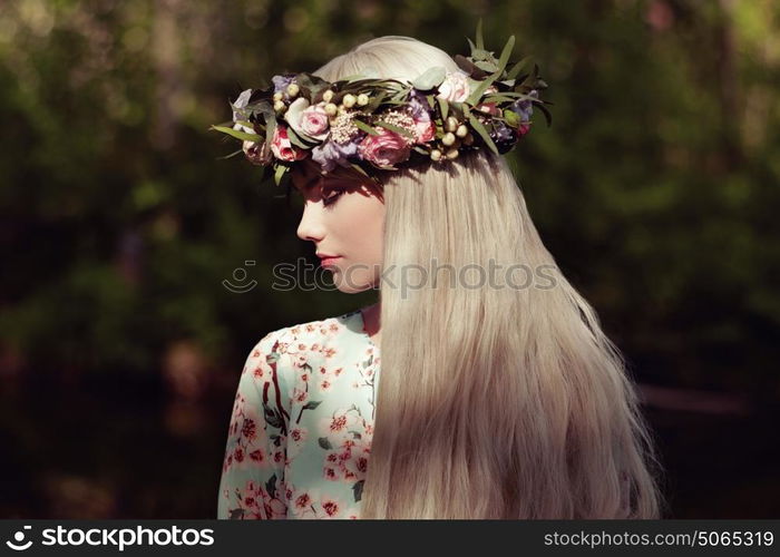 Beautiful blonde woman with flower wreath on her head. Beauty girl with flowers hairstyle. Girl in a summer forest. Fashion photo