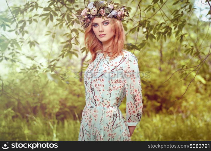 Beautiful blonde woman with flower wreath on her head. Beauty girl with flowers hairstyle. Girl in a summer forest. Fashion photo