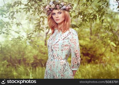 Beautiful blonde woman with flower wreath on her head. Beauty girl with flowers hairstyle. Girl in a summer forest. Fashion photo