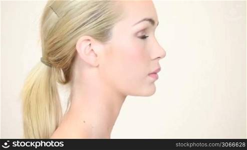 Beautiful blonde woman with her hair tied back standing smiling with her head turned slightly to the side