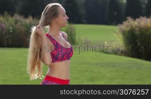 Beautiful blonde woman with pony tail letting her long hair down after work out in the park