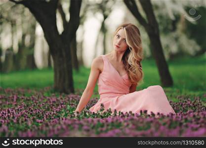 Beautiful blonde young woman in colorful flowers. girl with make-up and hairstyle in pink dress in blossoming spring park. woman&rsquo;s day.. Beautiful blonde young woman in colorful flowers. girl with make-up and hairstyle in pink dress in blossoming spring park. woman&rsquo;s day