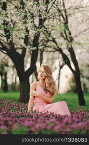 Beautiful blonde young woman in colorful flowers. girl with make-up and hairstyle in pink dress in blossoming spring park. woman&rsquo;s day.. Beautiful blonde young woman in colorful flowers. girl with make-up and hairstyle in pink dress in blossoming spring park. woman&rsquo;s day