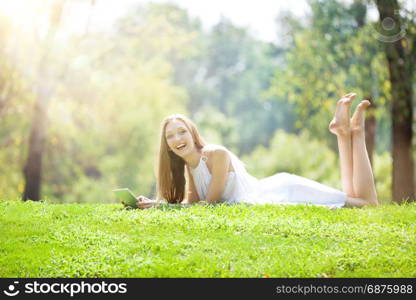 Beautiful Blonde Young Woman Lying with Laptop on the Beautiful Green Meadow in the Bright Sunny Day