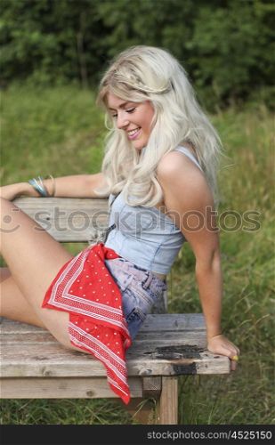 Beautiful blonde young woman sitting on a wooden bench outdoors