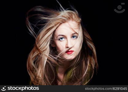 Beautiful blue-eyed woman with hair fluttering in wind on black background, fashion look