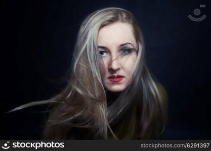 Beautiful blue-eyed woman with hair fluttering in wind on black background, fashion look