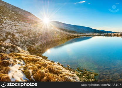 Beautiful blue lake in the mountains, morning sunrise time. Landscape with shining sun