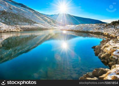 Beautiful blue lake in the mountains, morning sunrise time. Landscape with snow shining sun