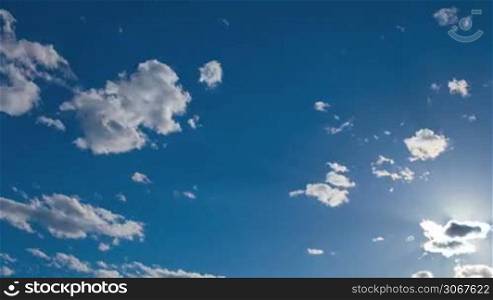 Beautiful blue sky background with fluffy white clouds and sun flare where the sun is shining out from behind a small cloud to the right of the frame