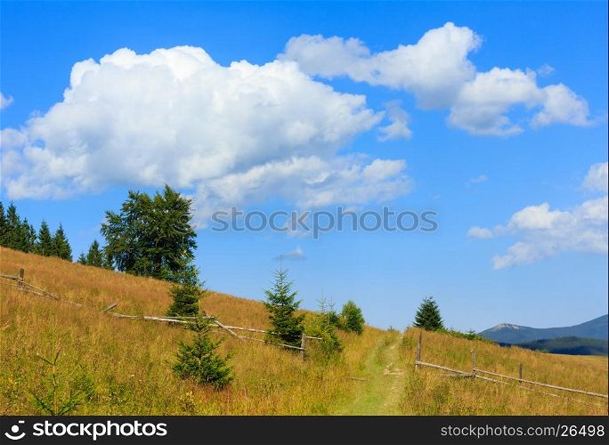 Beautiful blue sky with white cumulus clouds over summer Carpathian mountain hill with rural road and fence (Ukraine, Verkhovyna district, Ivano-Frankivsk region).