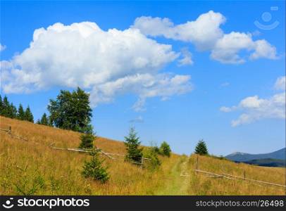 Beautiful blue sky with white cumulus clouds over summer Carpathian mountain hill with rural road and fence (Ukraine, Verkhovyna district, Ivano-Frankivsk region).
