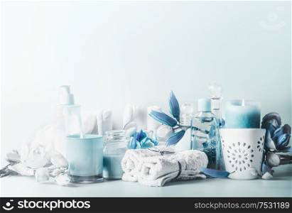 Beautiful blue white spa composition. Various cosmetic products with burning candles and flowers on table at light background. Skin care setting. Modern beauty concept