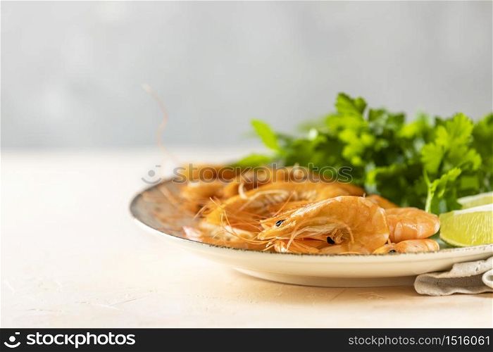 Beautiful boiled large shrimp in light ceramic plate with parsley and lime on pink concrete table surface. Fresh seafood ingredient - shrimp tails ready for cooking.