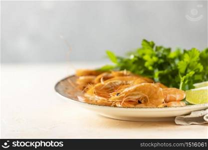 Beautiful boiled large shrimp in light ceramic plate with parsley and lime on pink concrete table surface. Fresh seafood ingredient - shrimp tails ready for cooking.