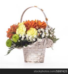 Beautiful bouquet of bright flowers in white basket on white tablecloth. Flowers in a basket