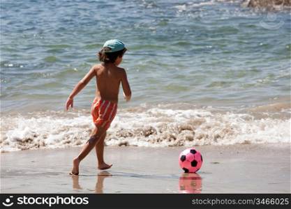 Beautiful boy with a soccer ball playing in the beach