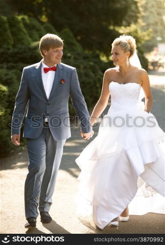 Beautiful bride and groom holding hands while walking at park