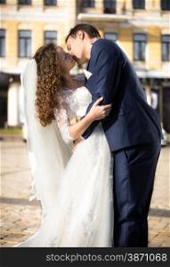 Beautiful bride and groom passionately kissing on street at sunny day