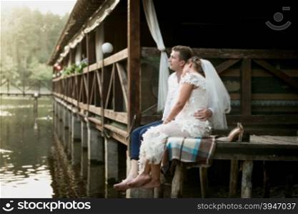 Beautiful bride and groom sitting on the pier and looking at river and forest