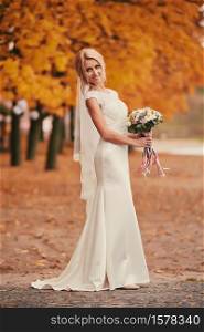Beautiful bride in luxury white long dress with wedding bouquet in autumn park on wedding day.. Beautiful bride in luxury white long dress with wedding bouquet in autumn park on wedding day