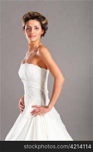 beautiful bride is standing in wedding dress on grey background and looking at camera