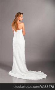 beautiful bride is standing in wedding dress on grey background, view from behind